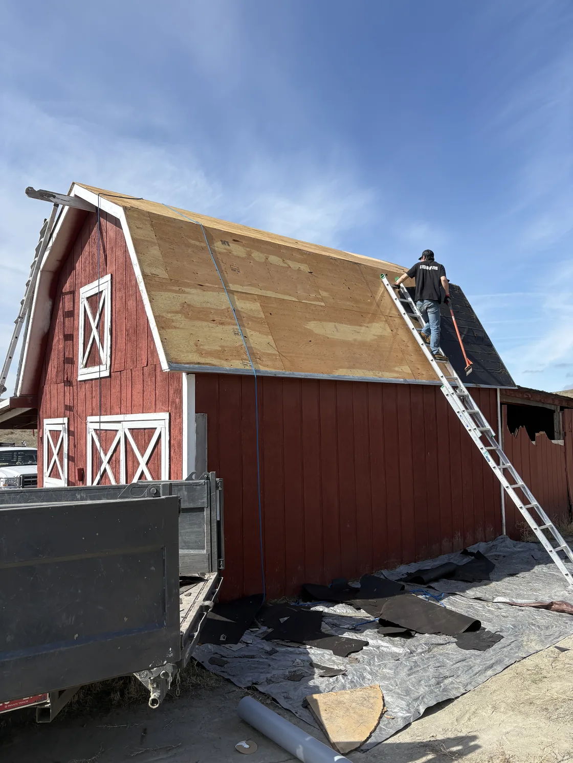 Red barn during roof replacement, with exposed roof decking and a ladder at the roof edge.