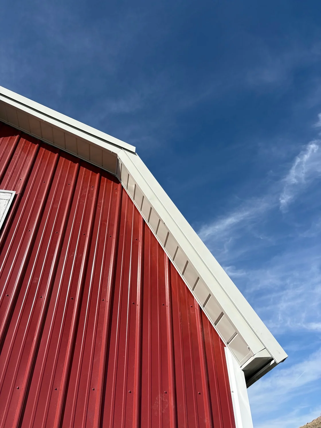 After soffit and fascia work: white panels and trim along the roof edge of the red Great Falls barn.