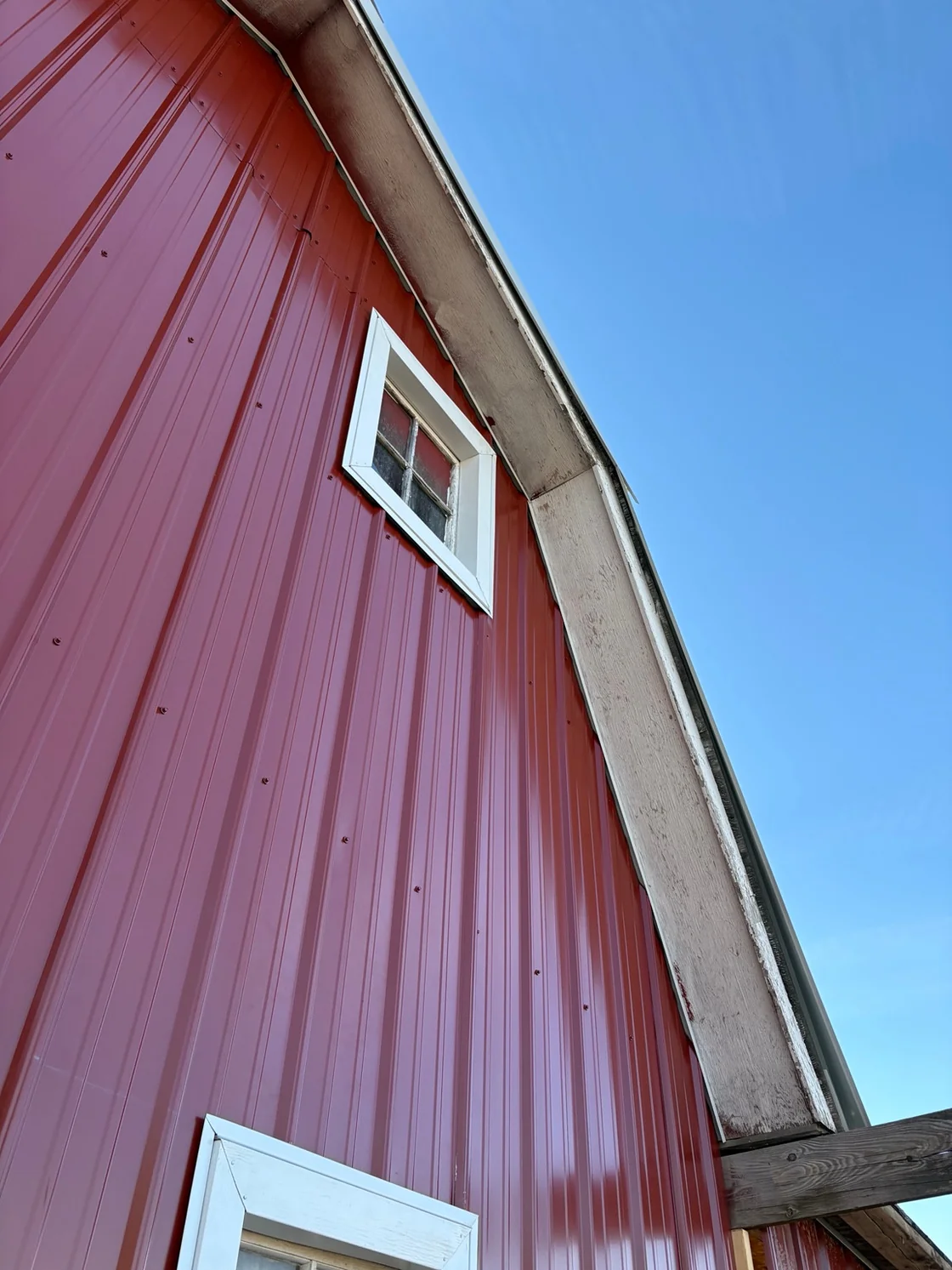 Before soffit and fascia work: weathered wood along the roof edge of the red Great Falls barn.