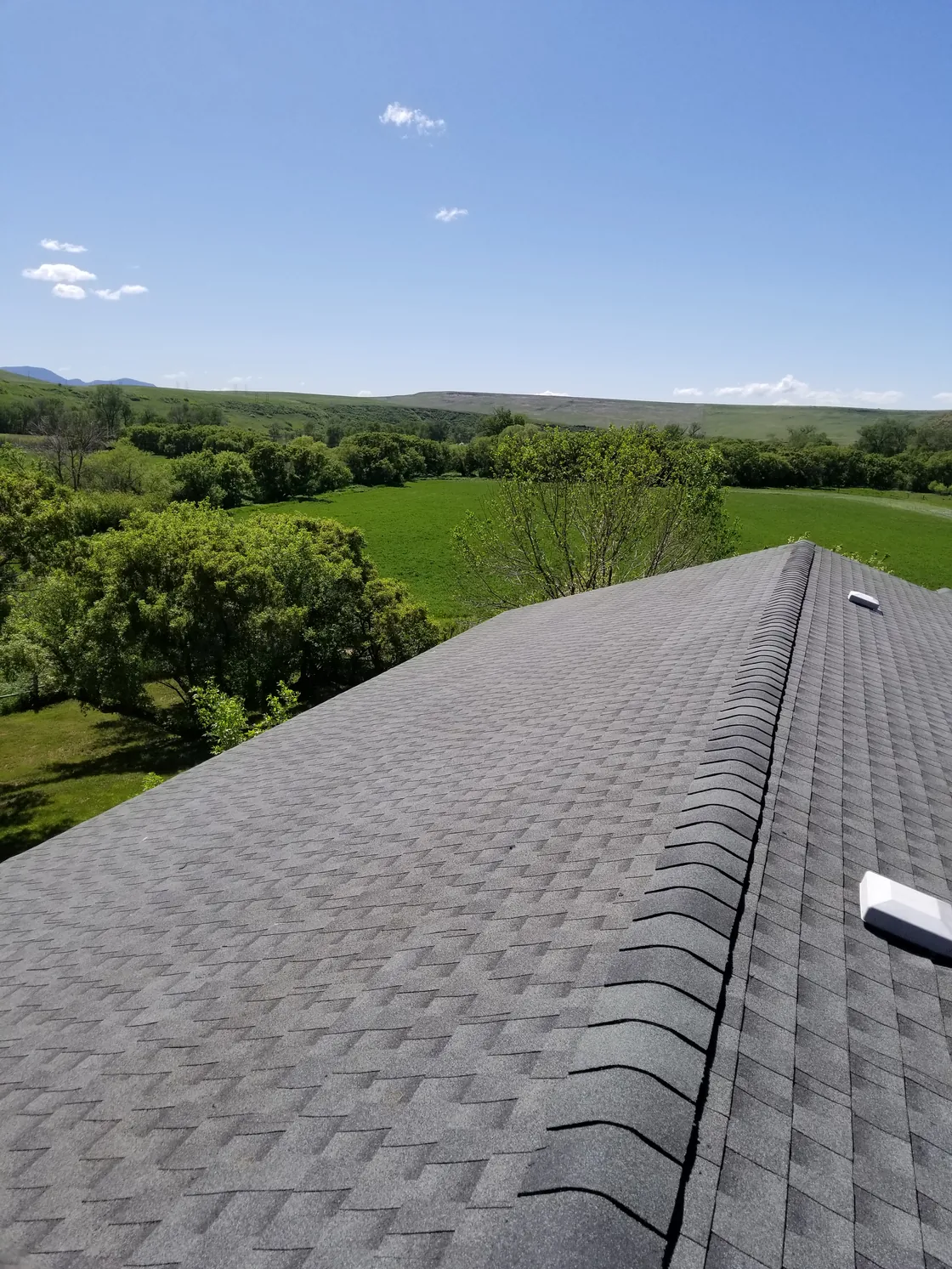 Finished gray shingle roof and capped ridge with a green landscape beyond.